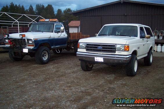 White Ford Bronco and a blue and white tow truck parked on gravel