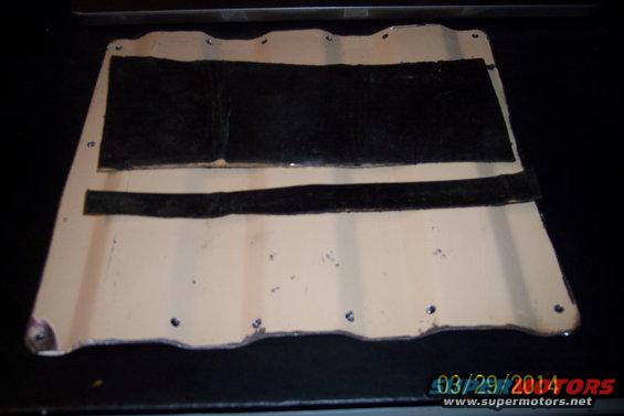 Beige metal panel with black fuzzy strips and screw holes