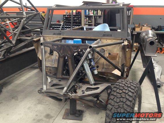 Off-road vehicle chassis with roll cage, engine, and suspension components visible. It's in a workshop setting
