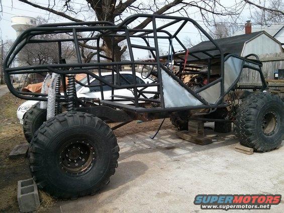 Custom off-road buggy frame with large tires and roll cage, sitting on blocks