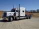 2003 Peterbilt 379 - A white 2003 Peterbilt 379 semi-truck is viewed from a three-quarter front angle under a clear blue sky.
