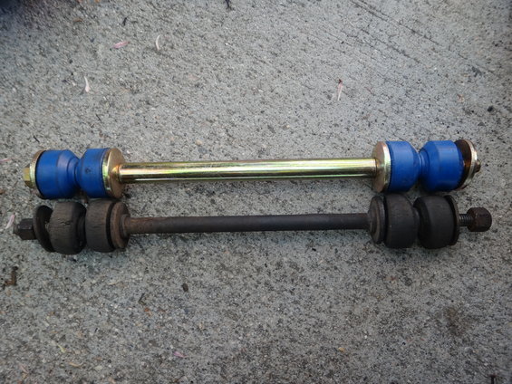 Two sway bar links on concrete; one is new with blue bushings and a gold bar, the other is old and rusted