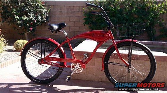 Red cruiser bicycle with a black seat, handlebars, and fenders, and a wire basket on the front
