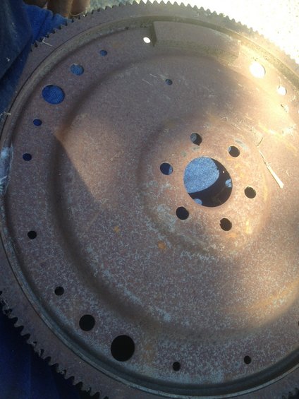 Rusted metal flywheel with gear teeth and bolt holes, close-up view