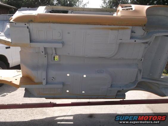 Car undercarriage, gray primer, on red lift arms, with a white truck visible to the left