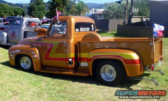Orange pickup truck with racing stripes and flags, parked next to a silver truck