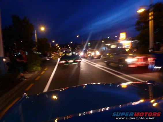 Cars driving down a street at night. Lights from buildings and street lamps illuminate the scene