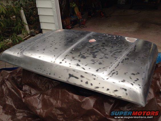 Bare metal car hood with primer spots, resting on a tarp