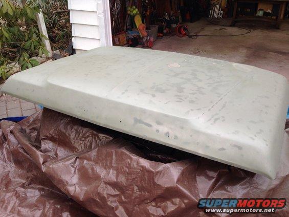 car hood covered in primer, resting on a tarp