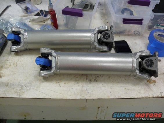 Two driveshafts on a workbench with blue protective caps