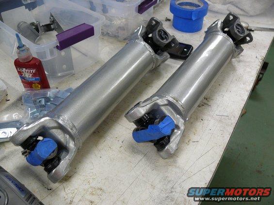 Two silver driveshafts with blue tape on U-joints, on a workbench with Loctite