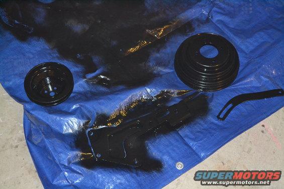 Black painted pulleys and bracket on a blue tarp with overspray