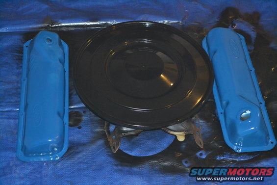 Two blue valve covers and a black air cleaner assembly on a blue tarp