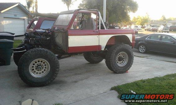 Red and white 1968 Ford Bronco, lifted with large tires, front fender removed