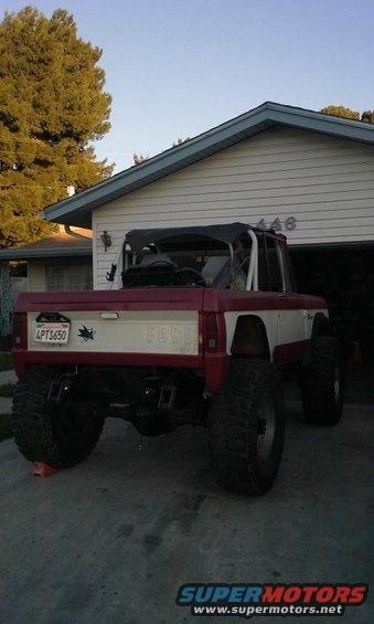 Red and white Ford Bronco with a soft top, lifted suspension, and large tires, viewed from the rear