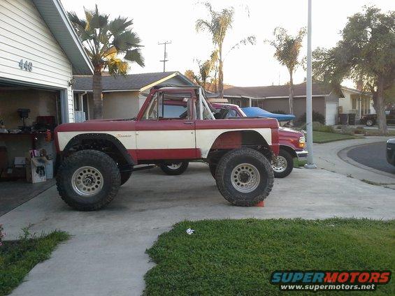 Side view of a lifted red and white 1968 Ford Bronco with large tires
