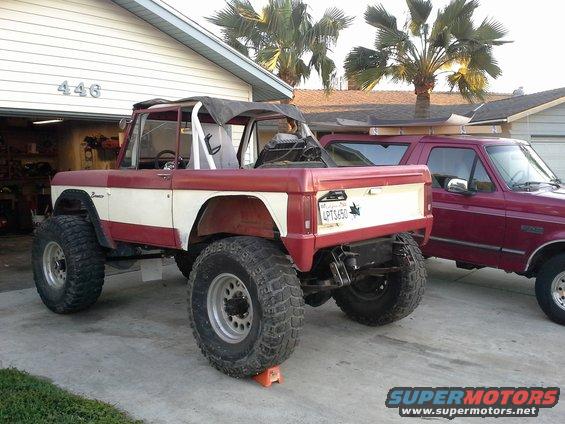 Red and white Ford Bronco with large tires parked in a driveway