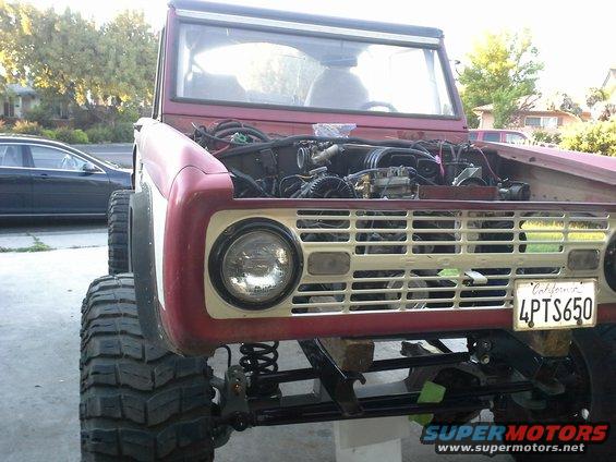 Front view of a red 1968 Ford Bronco with its hood open, showing the engine. It has large off-road tires and a California license plate reading 4PTS650