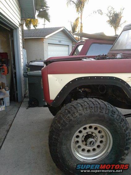 1968 Ford Bronco fender with off-road tire and suspension visible. Another Bronco is partially visible behind it