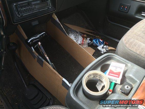 Truck interior showing a cardboard console insert, cigarette pack, lighter, and tape