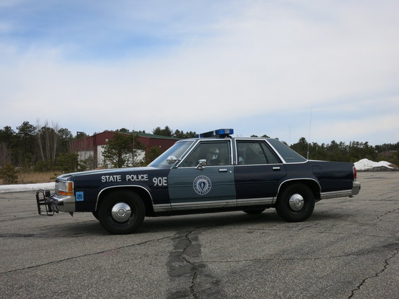 Dark blue and gray police car, side view, with "STATE POLICE 90E" text and a light bar