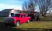 1978 Ford Bronco - A red pickup truck tows a rusty 1978 Ford Bronco on a trailer across a grassy yard.