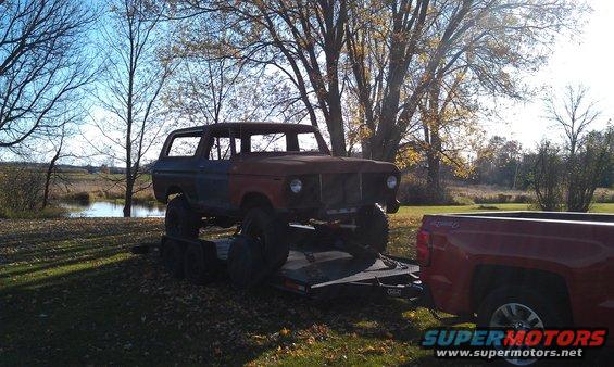 1978 Ford Bronco on trailer being towed by red pickup truck, rusty condition