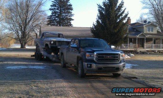 Older pickup truck on trailer towed by GMC pickup