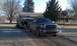 1978 Ford Bronco - A GMC pickup truck tows an older, unidentifiable pickup truck on a trailer through a rural setting.