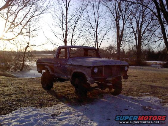 1970s Ford F-Series pickup truck, missing grille and windshield, parked in a snowy field