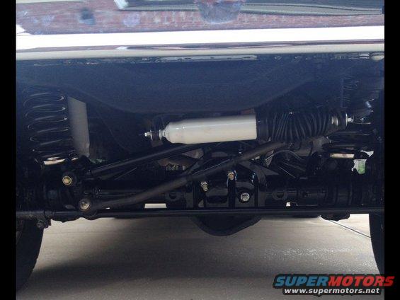 Undercarriage view of a vehicle's front suspension and steering components. Shows springs, shocks, and tie rods