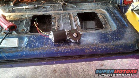 Blue tailgate interior with a removed window motor and wiring. Tools are visible