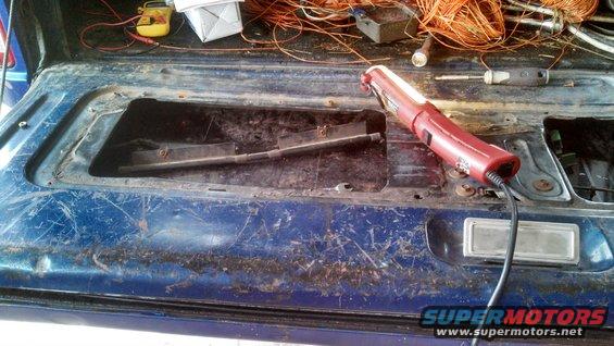 Blue tailgate interior with tools and wiring, showing rust and damage