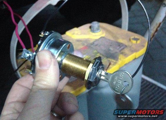 Hand holding a new ignition switch with a key in it, near a yellow car battery