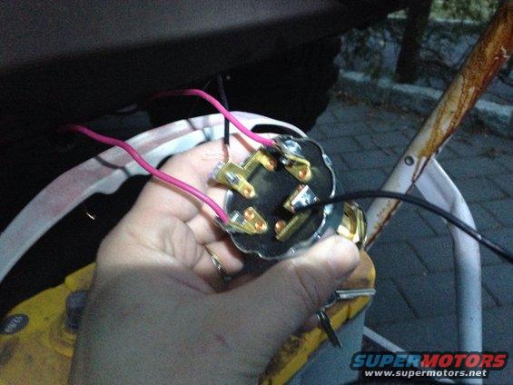 Hand holding a black ignition switch with pink and black wires connected