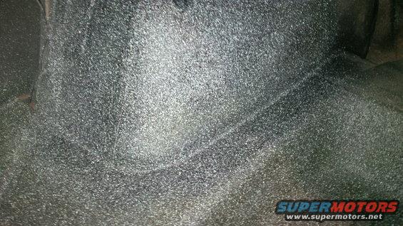 Underside of a vehicle, possibly the rear axle area. Shows textured undercoating