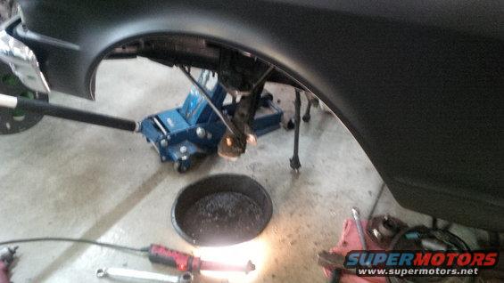 Car part under a jack with tools and oil pan