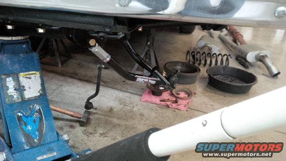 Car suspension components including a shock absorber, springs, and exhaust system laid out on a garage floor next to a blue jack