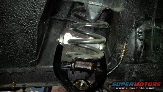 Close-up of a black suspension component with a coil spring and brake line
