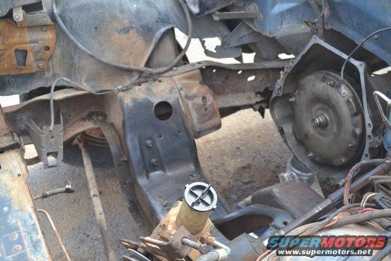 Disassembled vehicle engine bay showing frame, transmission, and various components. Some rust is visible