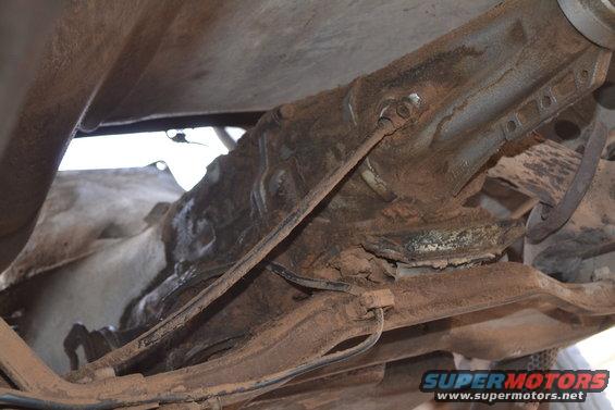 Underside of a rusty vehicle frame with suspension components and brake lines visible