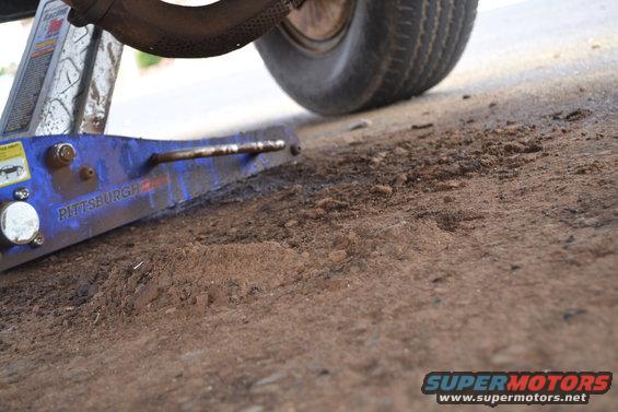 Blue car jack under a tire on dirt ground