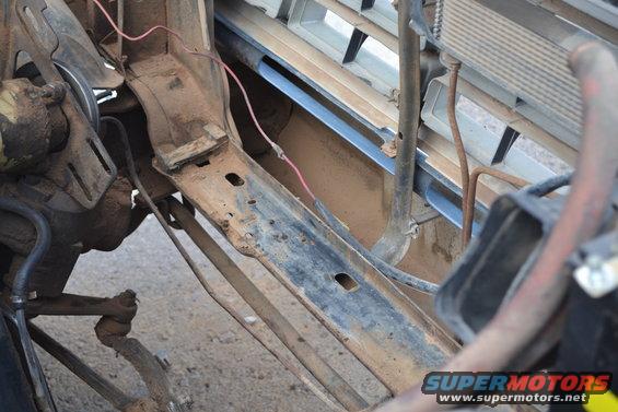 Rusty vehicle frame with radiator and fan visible. Grille slats are visible
