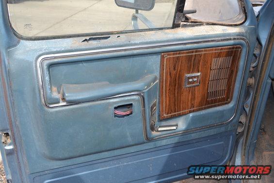 Blue truck door panel with wood grain trim and a broken door handle