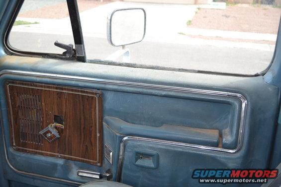 Blue interior door panel with wood grain trim and chrome accents. A square speaker grille is visible