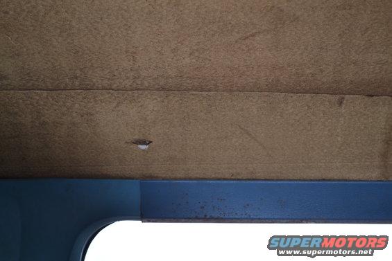 Brown textured headliner with a small tear, above a blue painted metal door frame and window opening