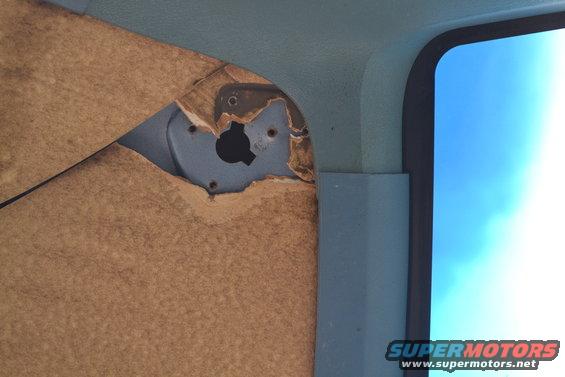 Torn brown door panel inside a vehicle, showing exposed blue metal and a black circular opening