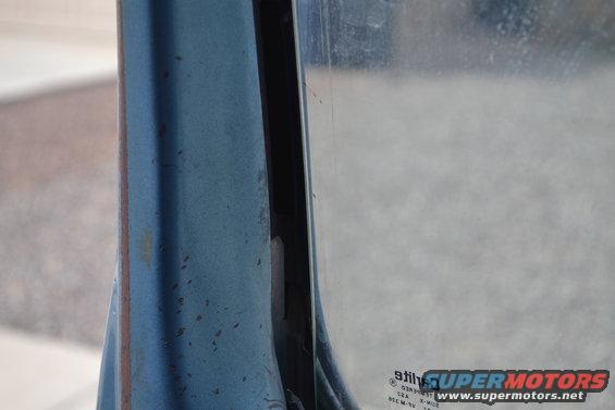 Blue painted metal door frame with rust spots next to a glass window showing a "Supermotors.net" watermark