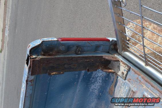 Close-up of a rusted blue truck bed corner showing a red taillight and metal bracing