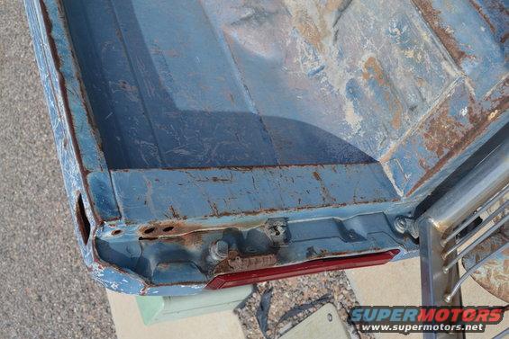 Close-up of a rusty blue truck bed corner with a red taillight